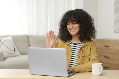 Happy woman waving hello during video call at table in room