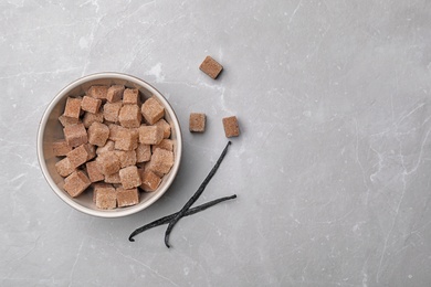 Photo of Bowl of aromatic vanilla lump sugar and sticks on grey background