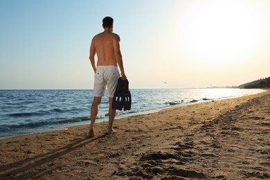 Photo of Man with flippers walking along sandy beach, back view. Space for text