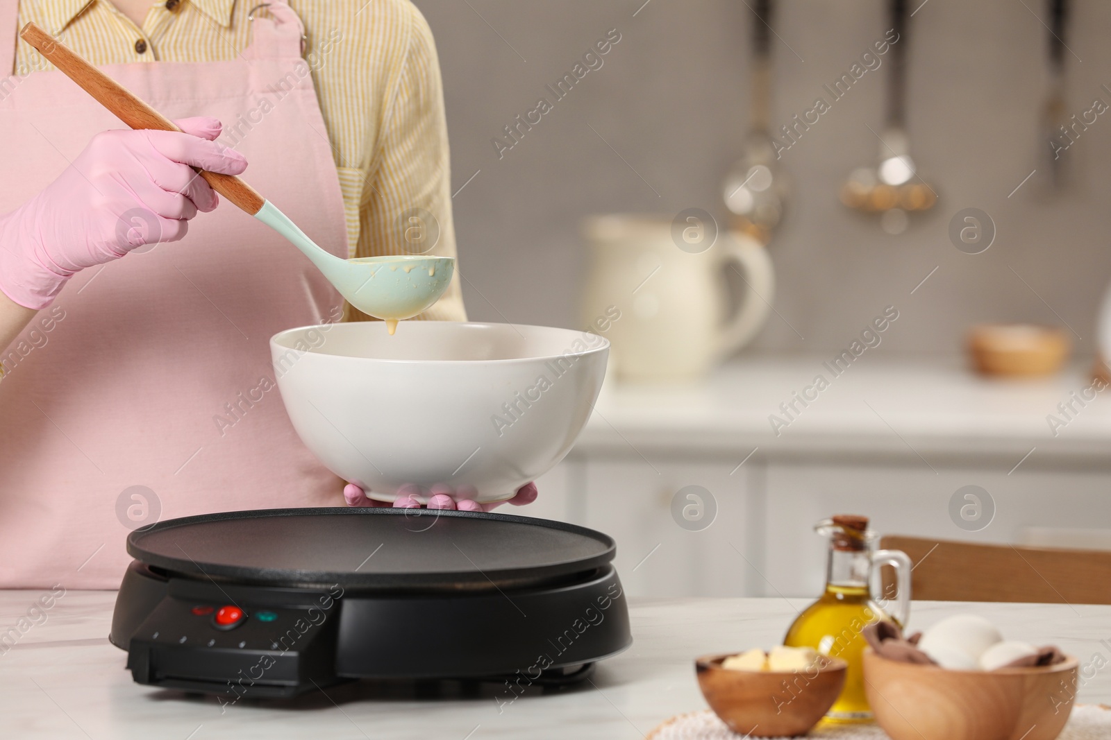 Photo of Woman cooking delicious crepe on electric pancake maker at white marble table in kitchen, closeup