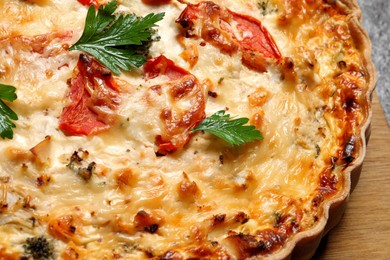 Tasty quiche with tomatoes, parsley and cheese on grey table, closeup