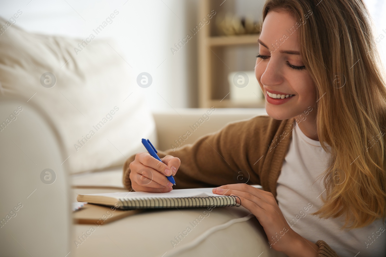 Photo of Happy woman writing letter on sofa at home