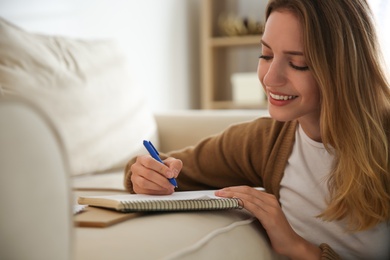 Photo of Happy woman writing letter on sofa at home