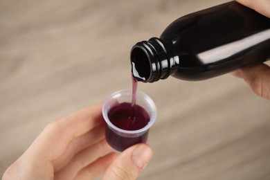 Woman pouring cough syrup into measuring cup on blurred background, closeup