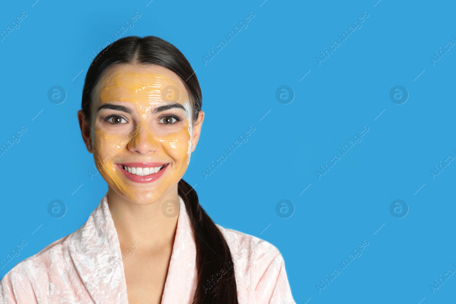 Photo of Young woman with cleansing mask on her face against color background, space for text. Skin care