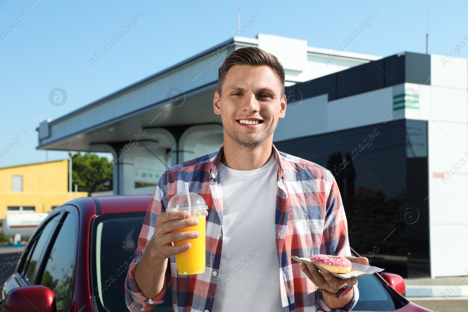 Photo of Young man with doughnut and juice near car at gas station