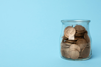 Photo of Glass jar with coins on light blue background, space for text
