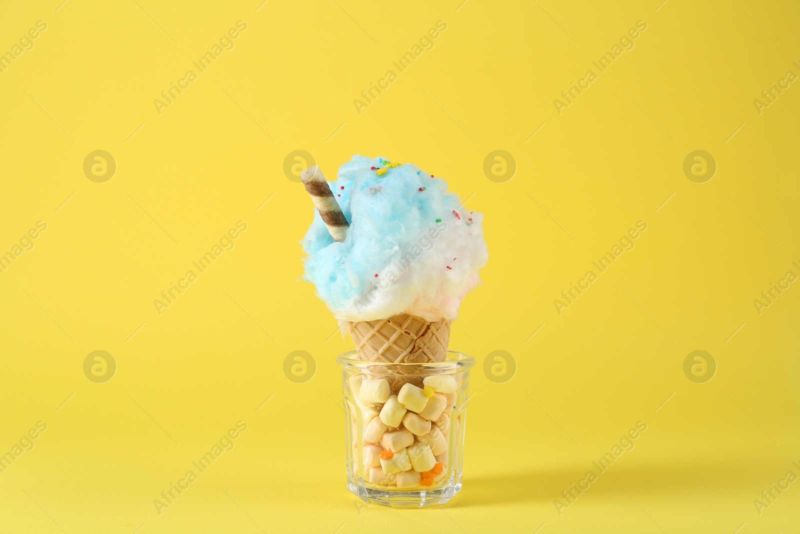 Photo of Sweet cotton candy in waffle cone on yellow background