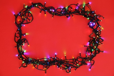 Glowing Christmas lights on color background, top view