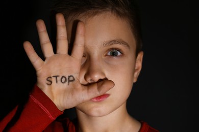 Photo of Abused little boy showing palm with word STOP on black background. Domestic violence concept