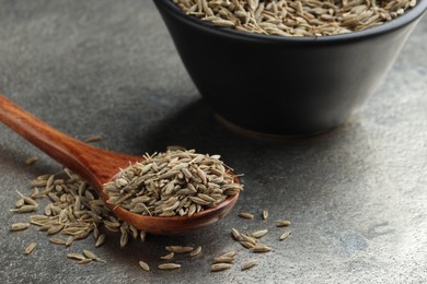 Photo of Spoon and bowl with caraway seeds on grey table, closeup