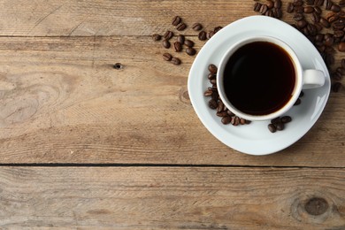 Photo of Cup of hot aromatic coffee and roasted beans on wooden table, flat lay. Space for text