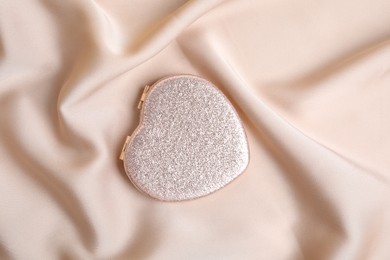 Photo of Stylish heart shaped cosmetic pocket mirror on rose gold fabric, top view