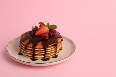Stack of tasty pancakes with fresh berries, chocolate sauce and mint on pink background. Space for text