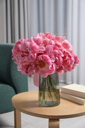 Beautiful bouquet of pink peonies in vase and books on wooden table indoors