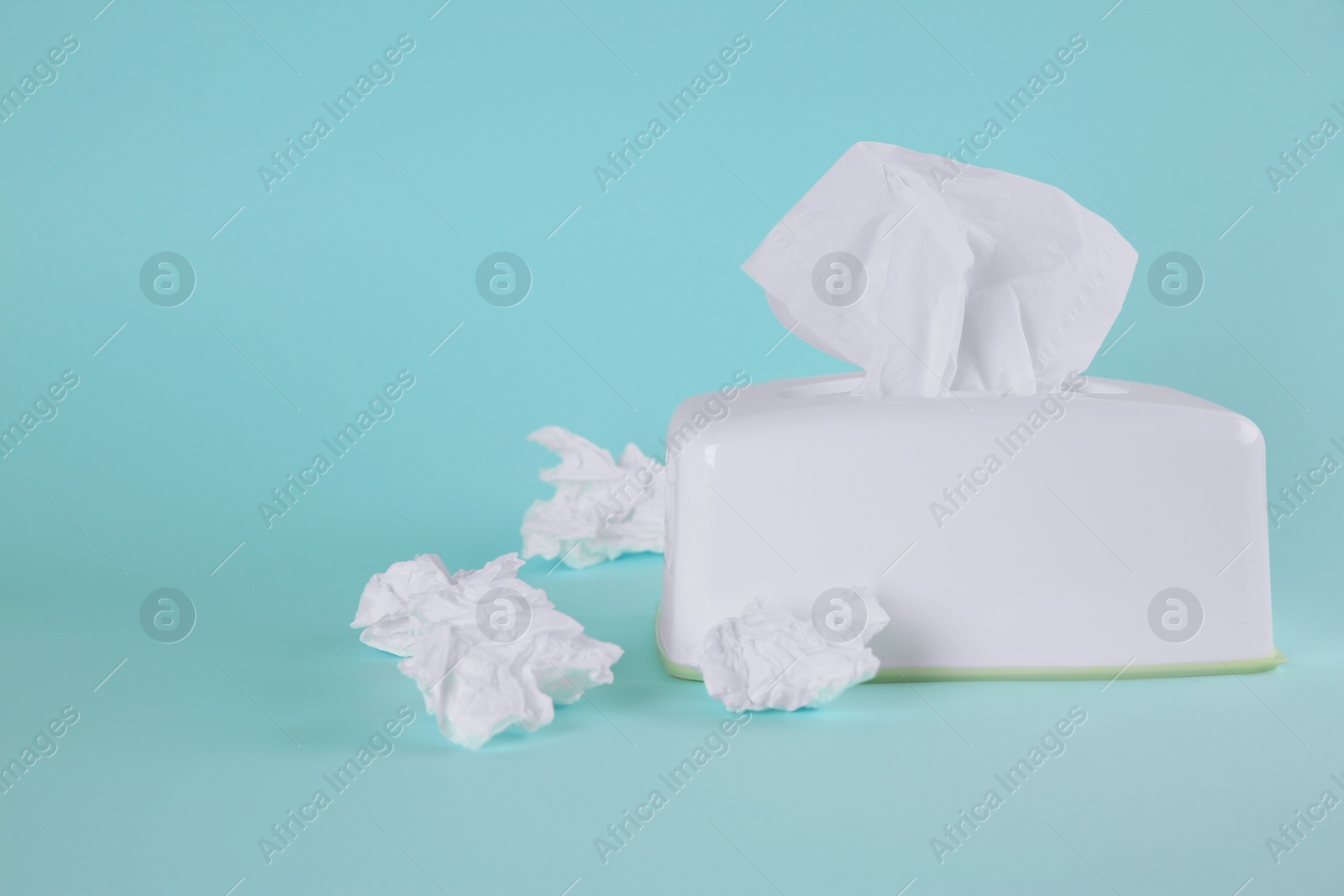 Photo of Used paper tissues and white holder on light blue background