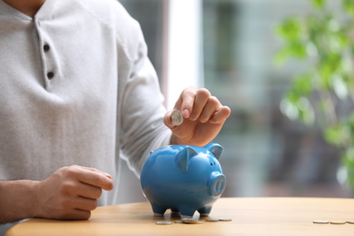 Photo of Man putting money into piggy bank at table, closeup. Space for text