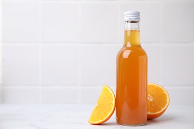 Photo of Delicious kombucha in glass bottle and orange on white table, space for text