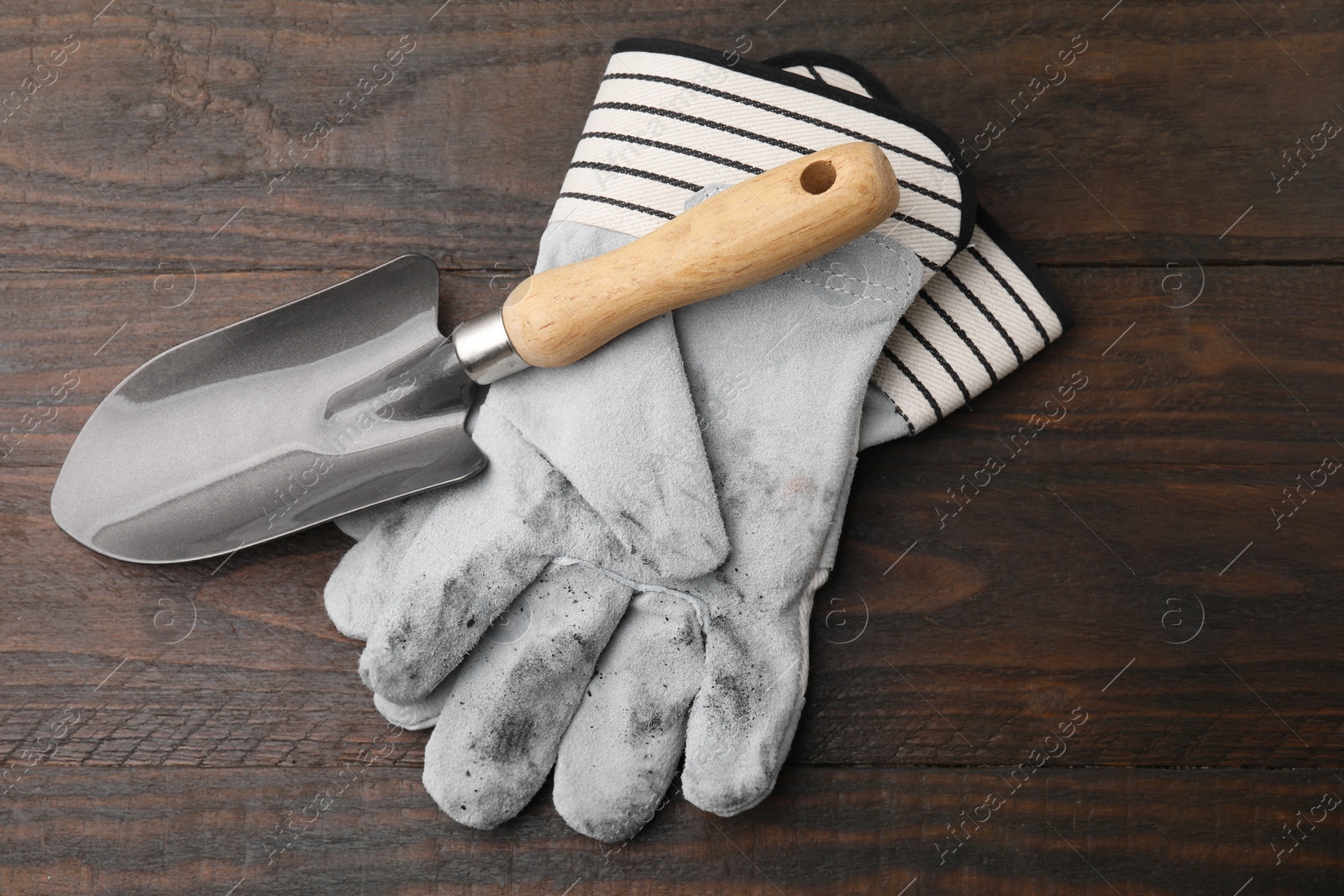 Photo of Pair of color gardening gloves and trowel on wooden table, top view