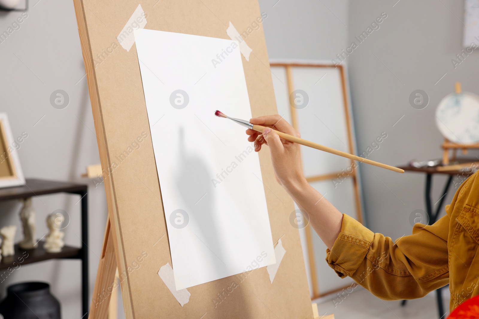 Photo of Woman painting on easel with paper in studio, closeup