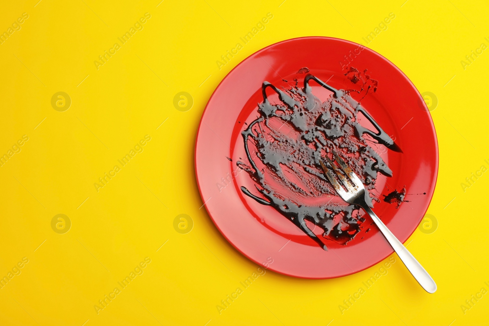 Photo of Dirty plate with food leftovers and fork on yellow background, top view. Space for text