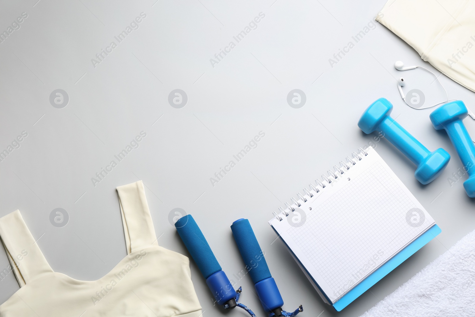 Photo of Flat lay composition with sportswear, notebook and dumbbells on light grey background, space for text. Gym workout plan