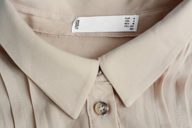Photo of White clothing label on beige blouse, closeup
