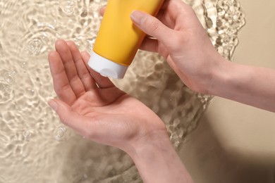 Woman applying face cleansing product onto hand against beige background, top view