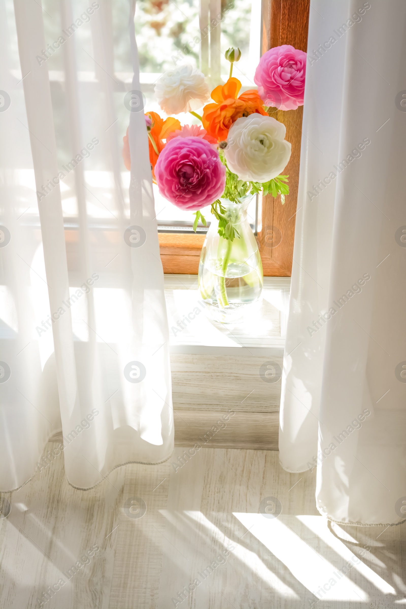 Photo of Bouquet of beautiful bright ranunculus flowers in glass vase indoors