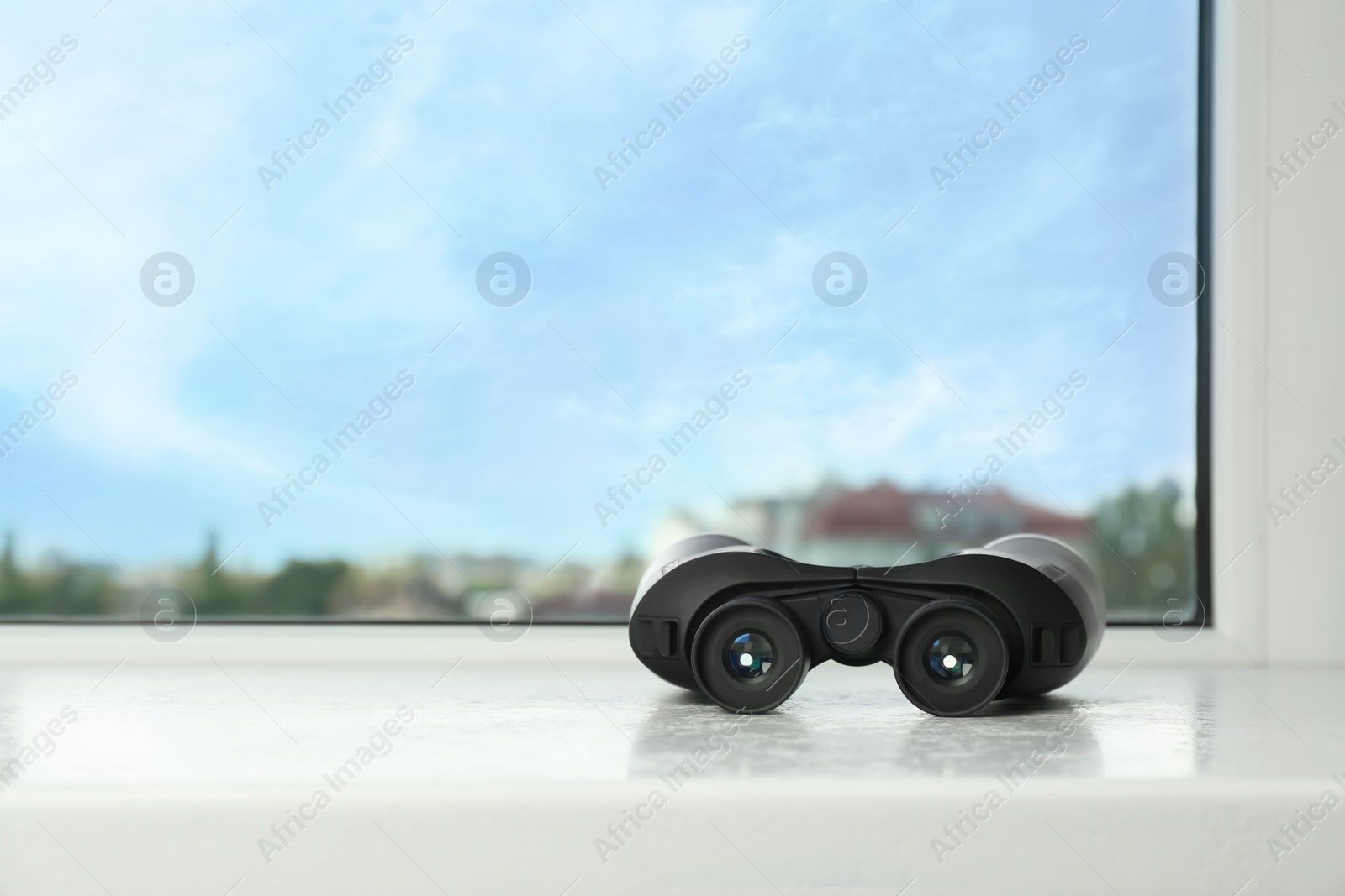 Photo of Black binoculars on white window sill. Space for text