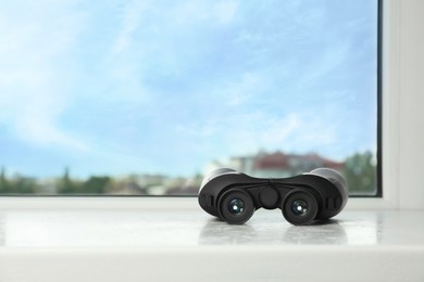 Photo of Black binoculars on white window sill. Space for text