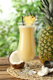 Photo of Tasty Pina Colada cocktail and ingredients on wooden table