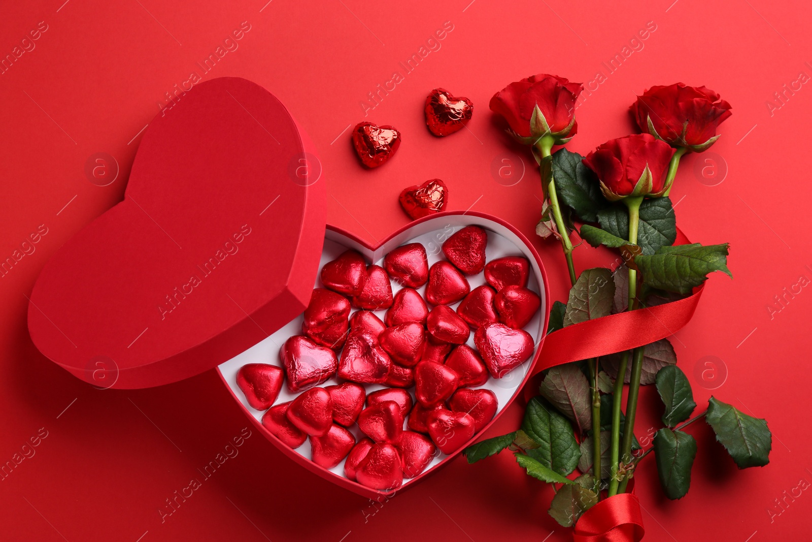 Photo of Heart shaped chocolate candies and bouquet on red background, flat lay
