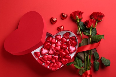 Photo of Heart shaped chocolate candies and bouquet on red background, flat lay