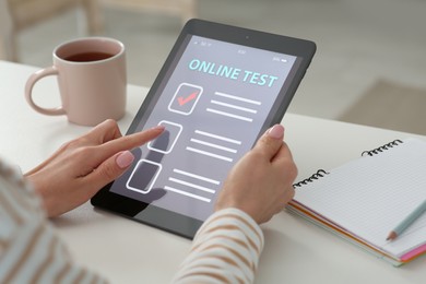 Photo of Woman taking online test on tablet at desk indoors, closeup