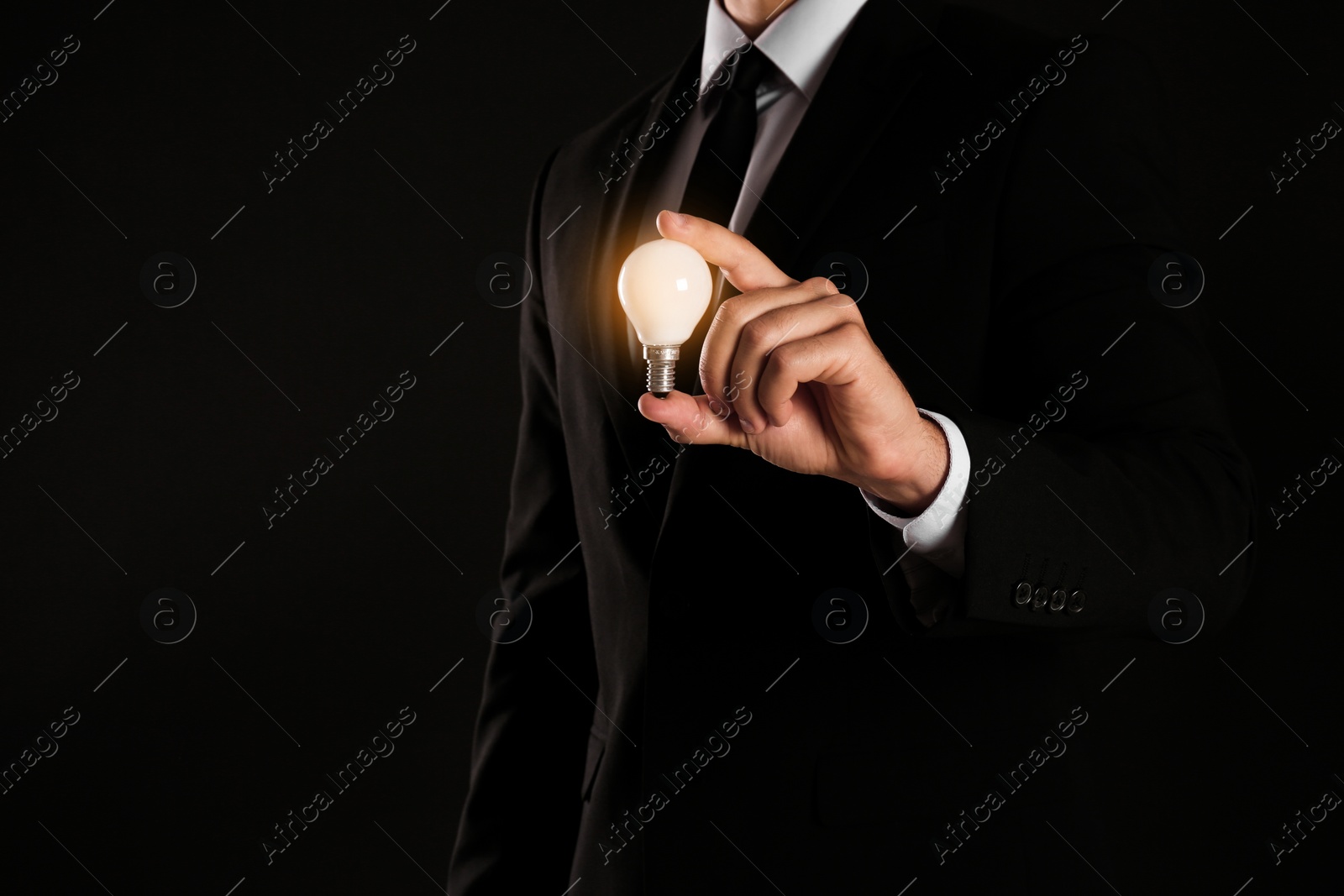 Photo of Businessman holding lamp bulb against dark background, closeup. Space for text