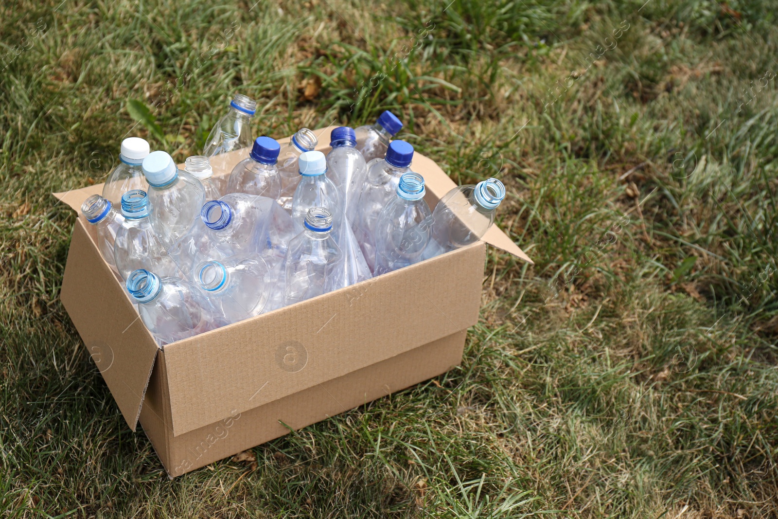 Photo of Cardboard box with used plastic bottles on grass. Recycling problem