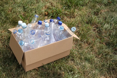 Photo of Cardboard box with used plastic bottles on grass. Recycling problem