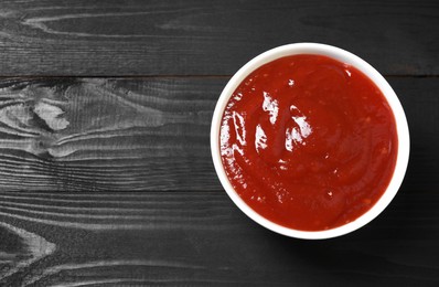 Delicious ketchup in bowl on black wooden table, top view with space for text. Tomato sauce