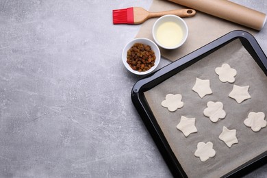 Photo of Parchment paper, baking pan with raw cookies and different ingredients on light grey table, flat lay. Space for text