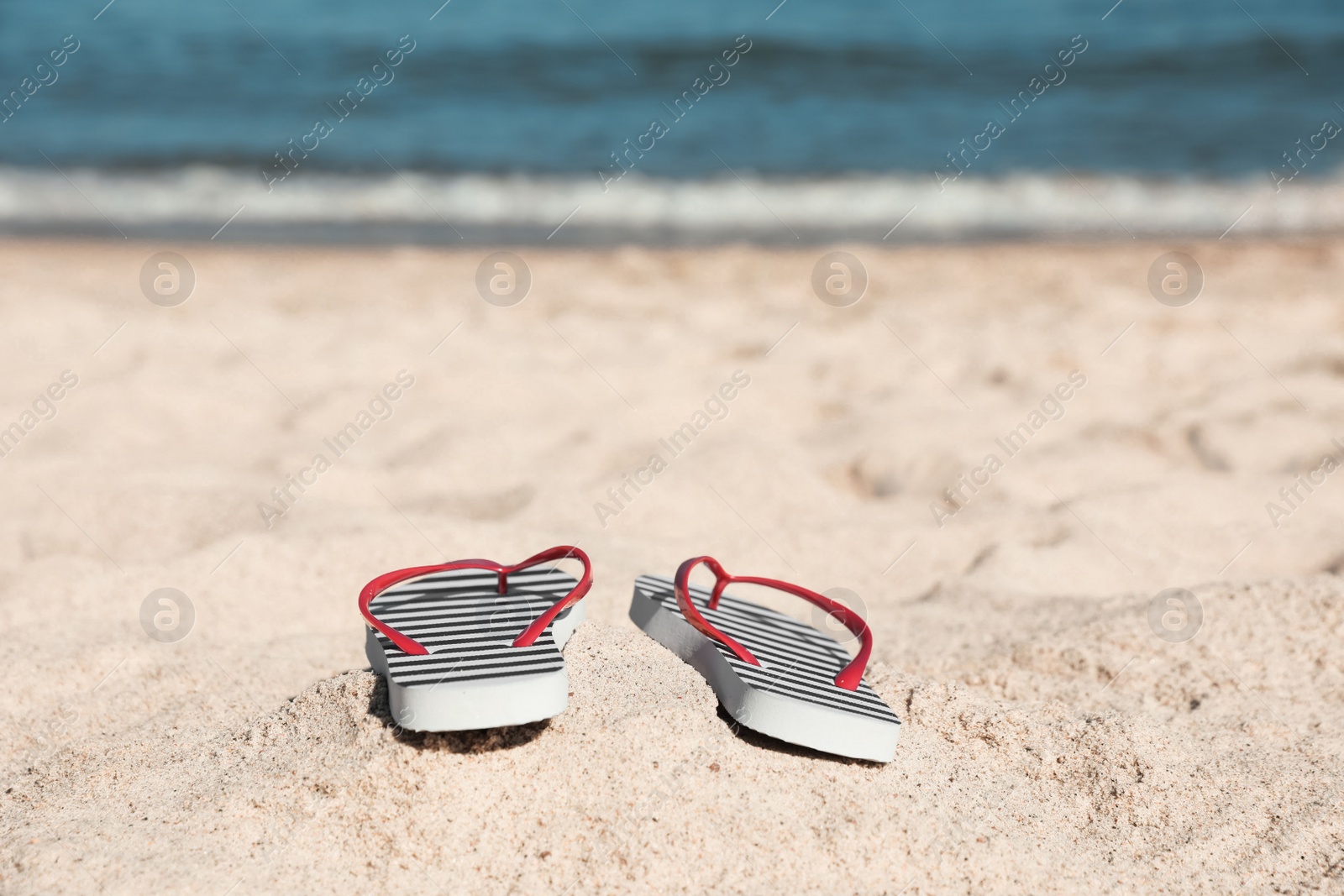 Photo of Striped flip flops on sandy beach near sea