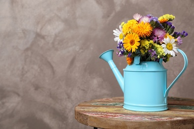 Watering can with beautiful wild flowers on table against grey background