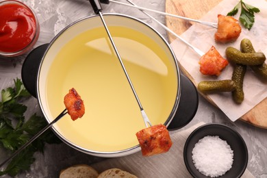 Fondue pot, forks with fried meat pieces, salt and other products on grey textured table, flat lay