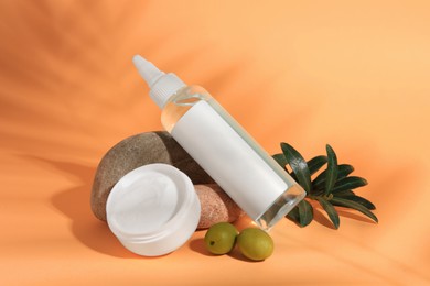 Cosmetic products and olives on orange background