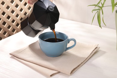 Photo of Pouring aromatic coffee from moka pot into cup at white wooden table, closeup