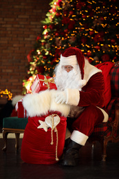 Santa Claus with gift sack near Christmas tree indoors