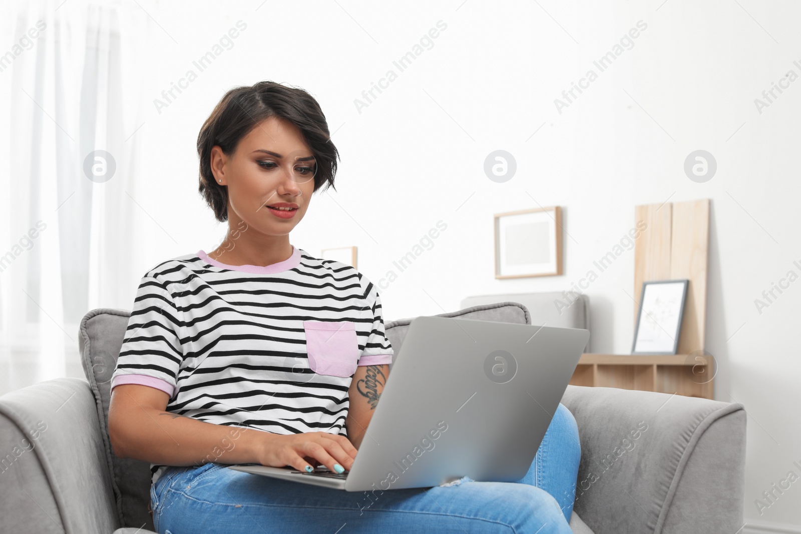 Photo of Young woman with modern laptop sitting in armchair at home