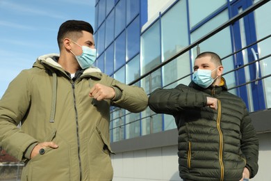 Photo of Men in masks greeting each other by bumping elbows outdoors