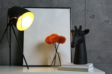 Photo of Stylish decor, vase with flowers, picture and desk lamp on white table near grey wall indoors. Interior design
