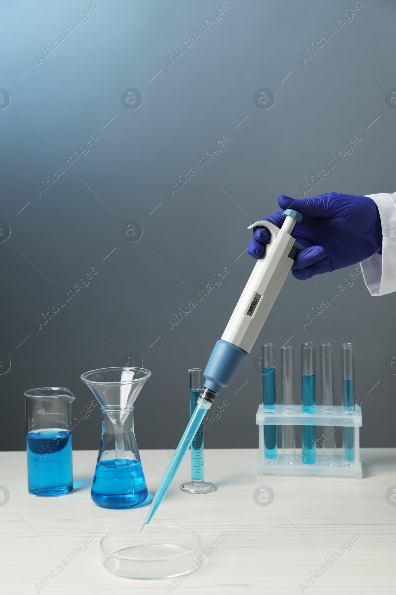 Photo of Laboratory analysis. Scientist dripping sample with micropipette into petri dish at white wooden table, closeup